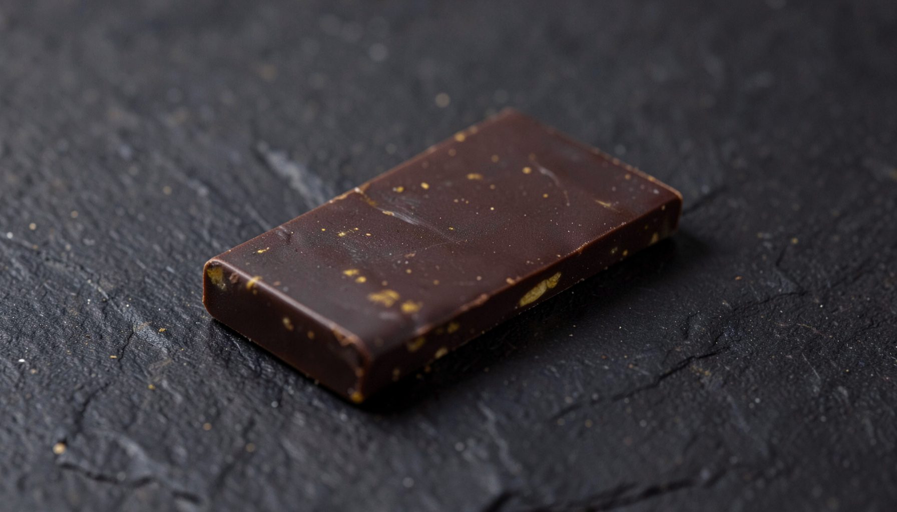 Artisan chocolate bar resting on dark slate, subtle golden highlights, rich browns and deep charcoal tones