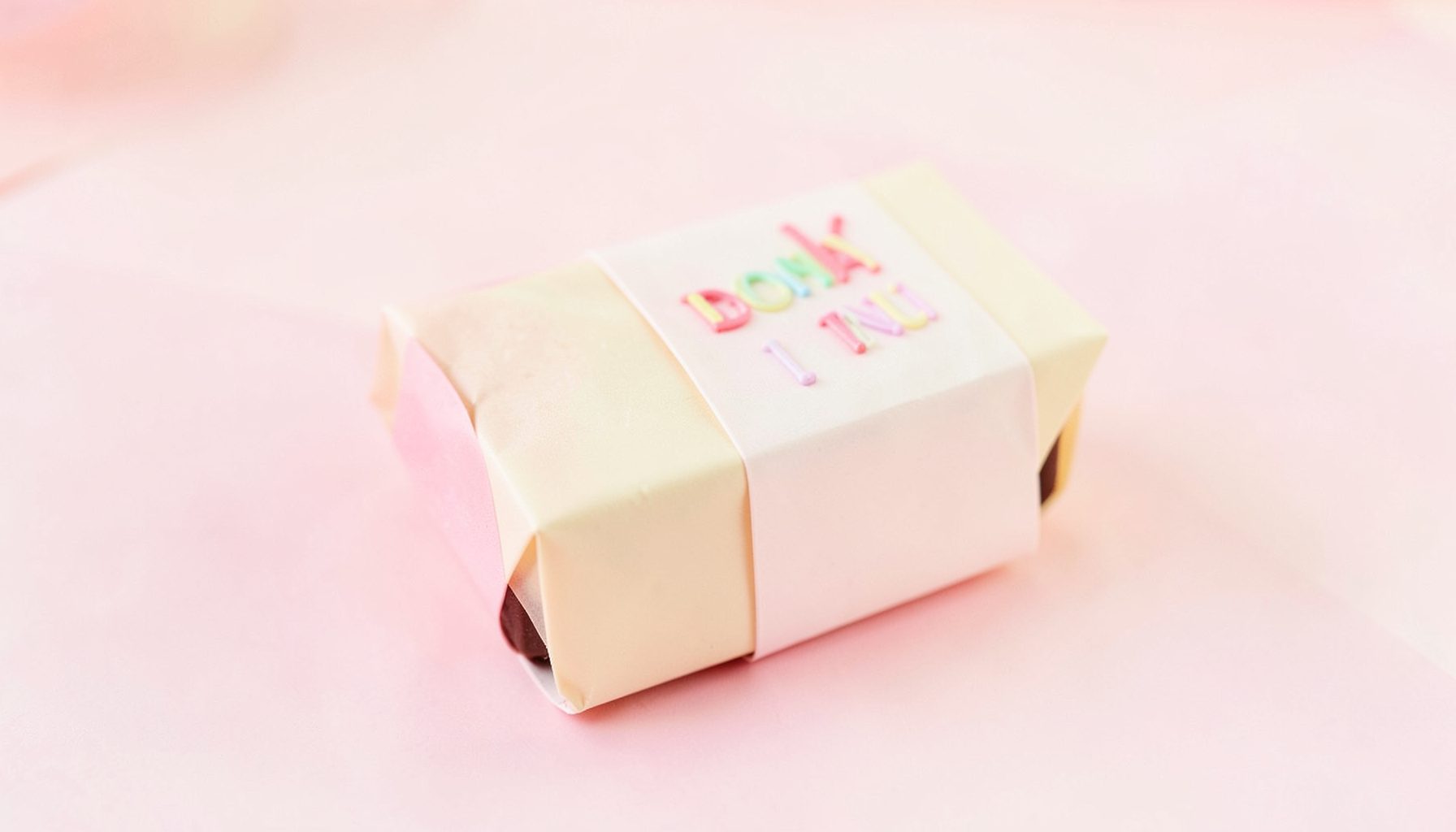 Chocolate bar wrapped in a warm cream and pink pastel package evoking a birthday cake theme, cheerful mood