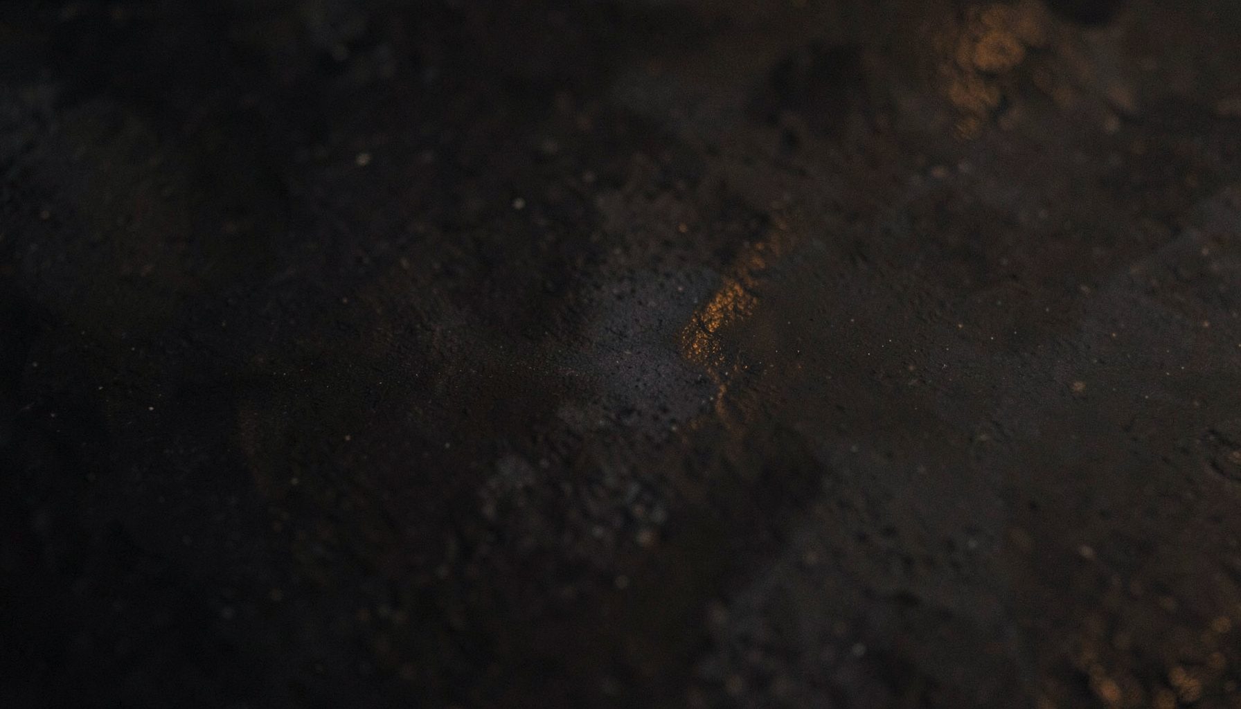 Dark textured surface with subtle warm highlights, moody and understated